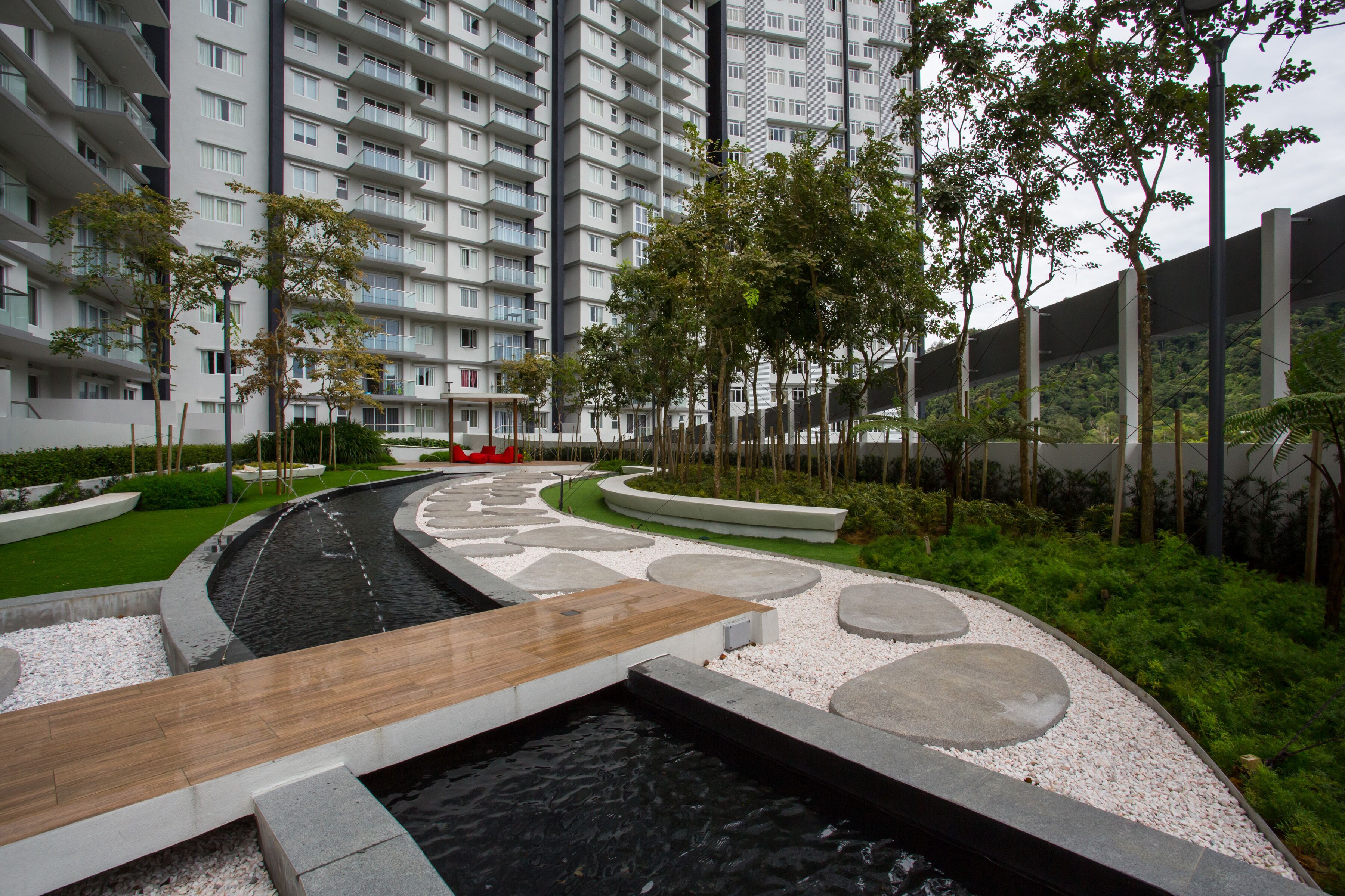 A modern residential building with a landscaped garden featuring a water feature, pathways, and greenery.