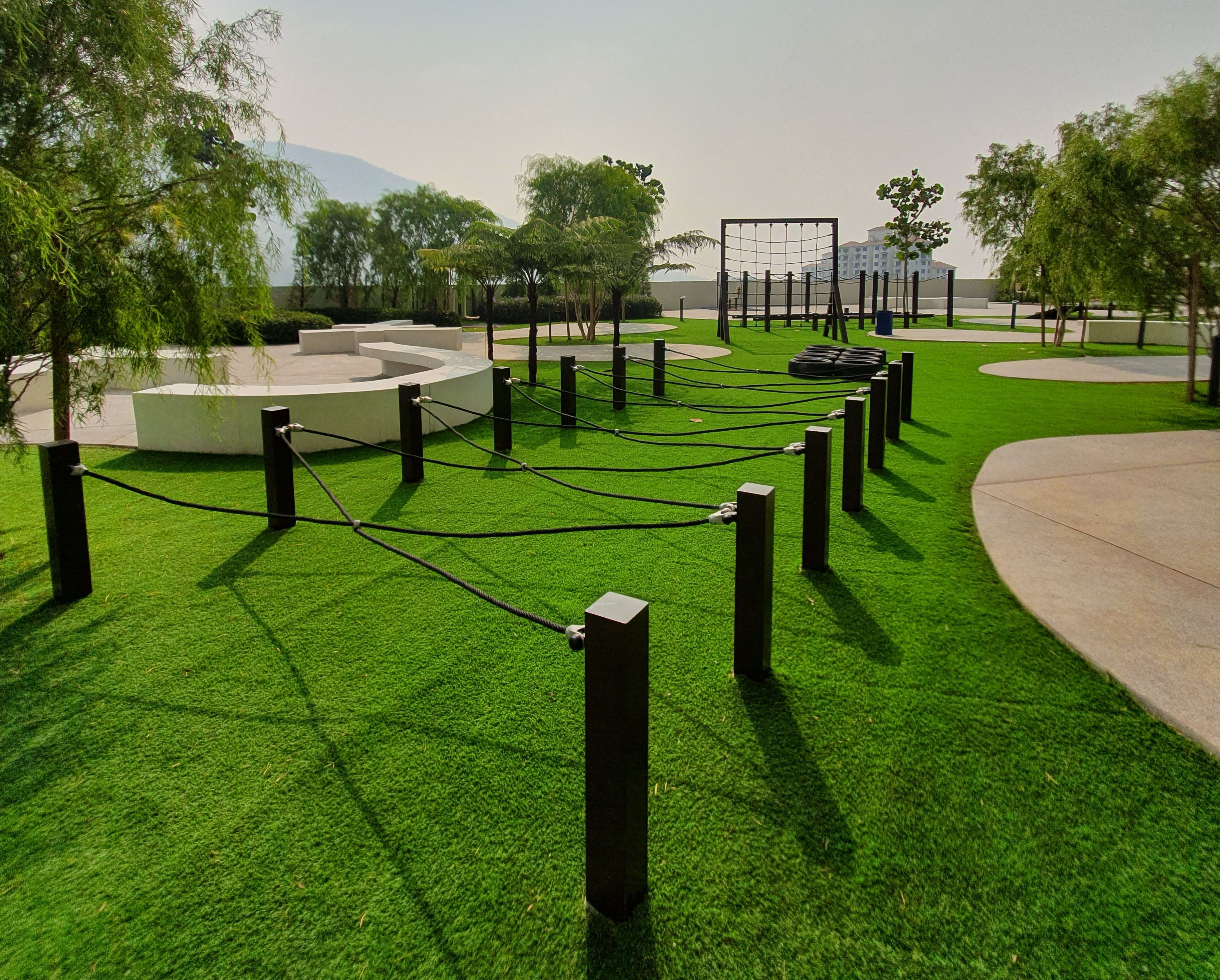 A landscaped area with a fenced sports facility, including a soccer goal, surrounded by trees and a concrete pathway.