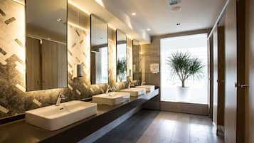 A modern bathroom with three sinks, large mirrors, and a potted plant.