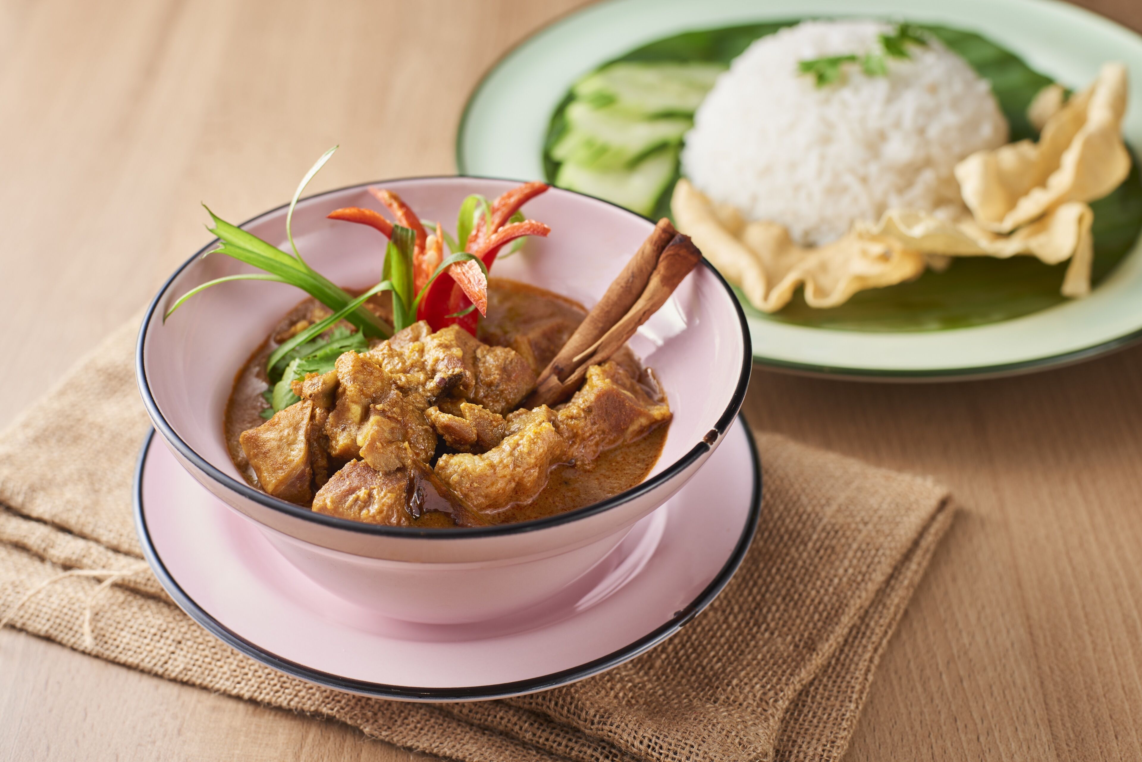 A bowl of curry with a side of rice and vegetables on a plate.