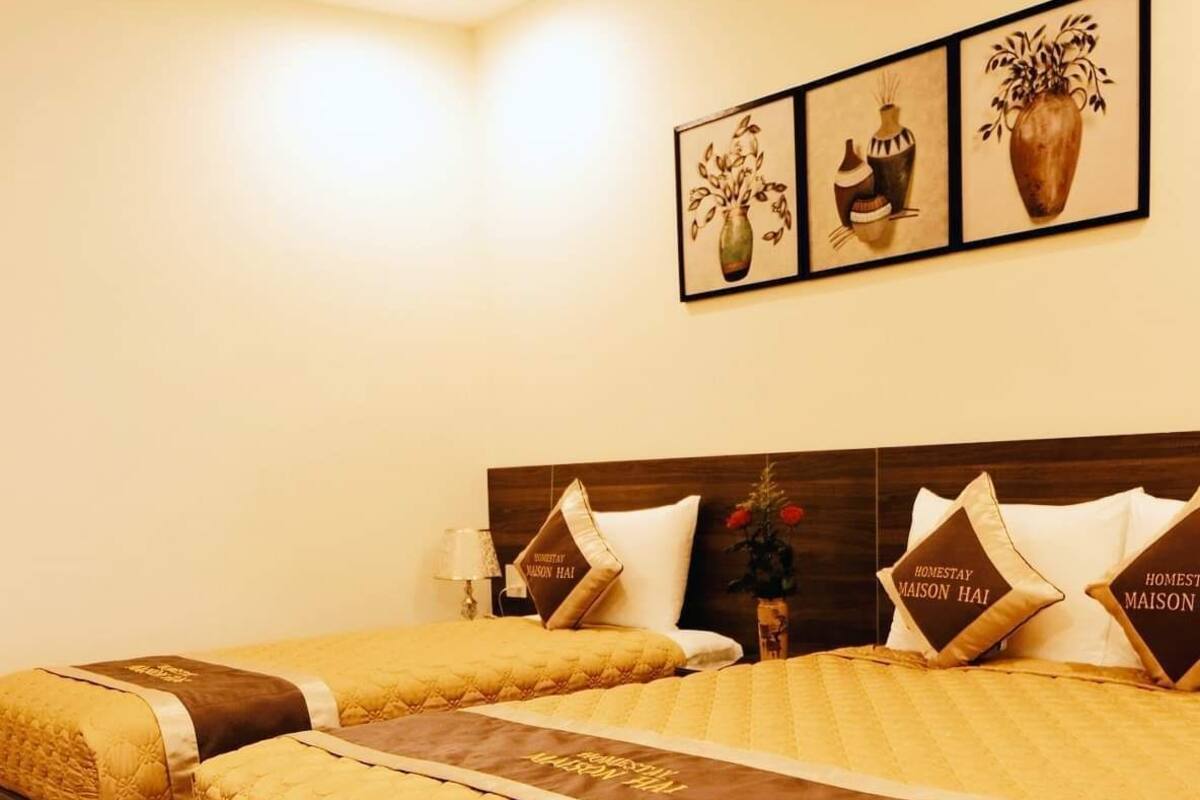 A hotel room with a large bed, two bedside tables, and a nightstand. There are three framed artworks on the wall above the bed.