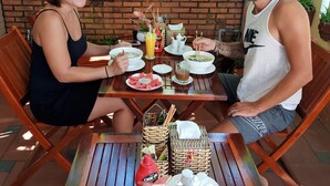A dining table with plates of food, a glass of juice, and a vase of flowers. - Maison Hai Homestay (Da Nang)