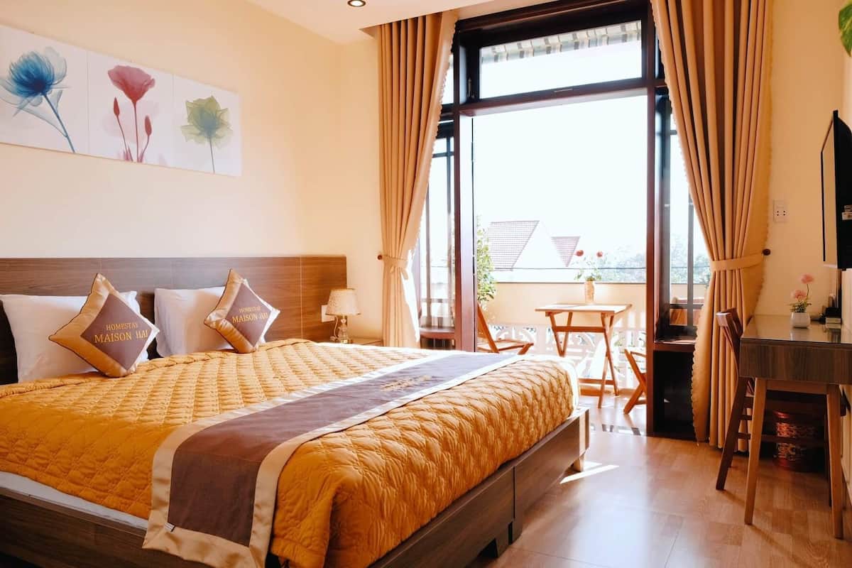A hotel room with a large bed, a desk, and a balcony with a table and chairs.