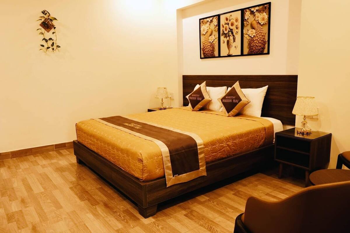 A hotel room with a large bed, two bedside tables, a chair, and a wall with three framed artworks.