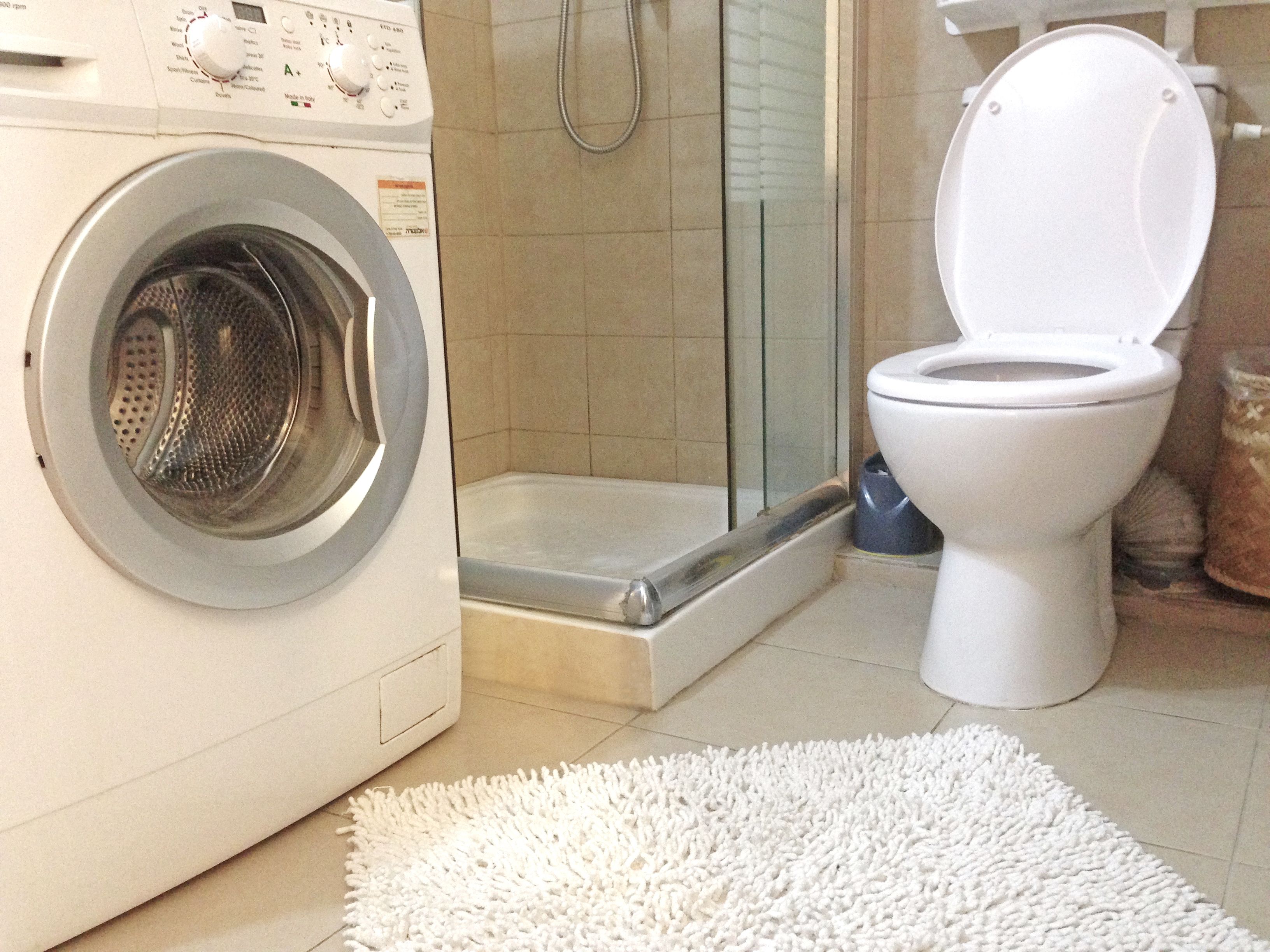 Casa de banho compacta com máquina de lavar roupa, sanita e zona de duche.