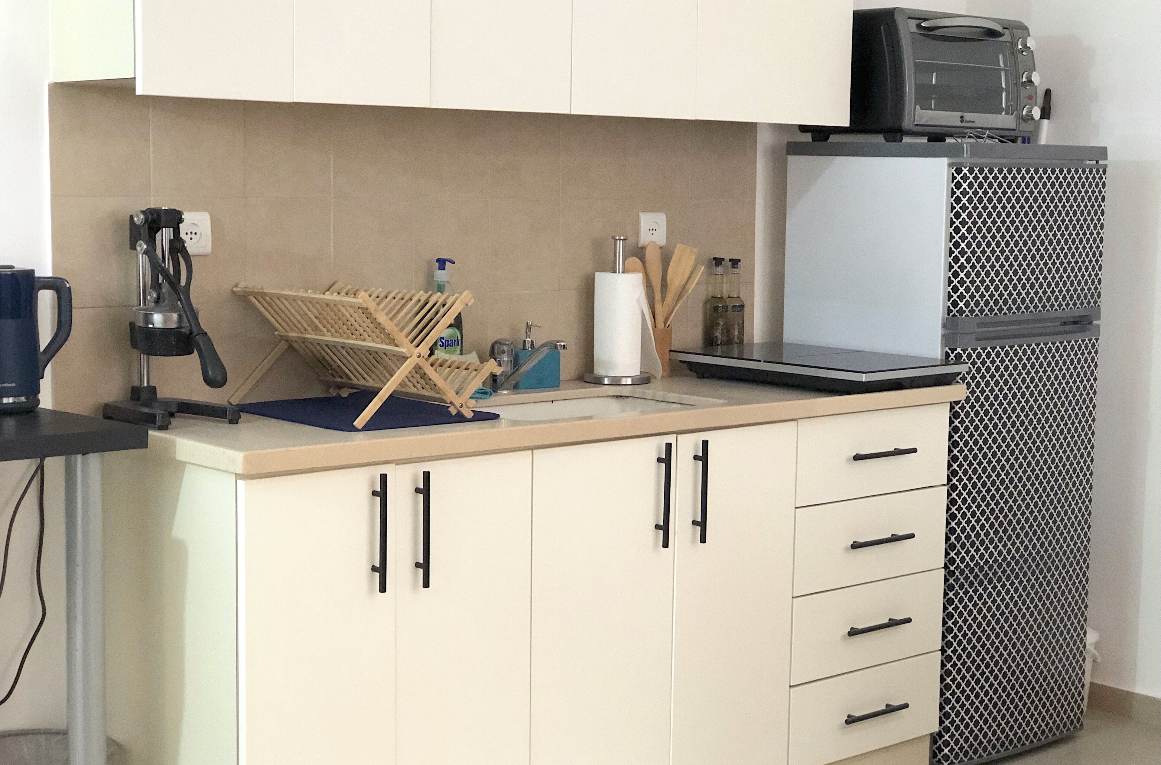A kitchen with a microwave, toaster, and a small refrigerator. There is a dish rack and a coffee machine on the counter.