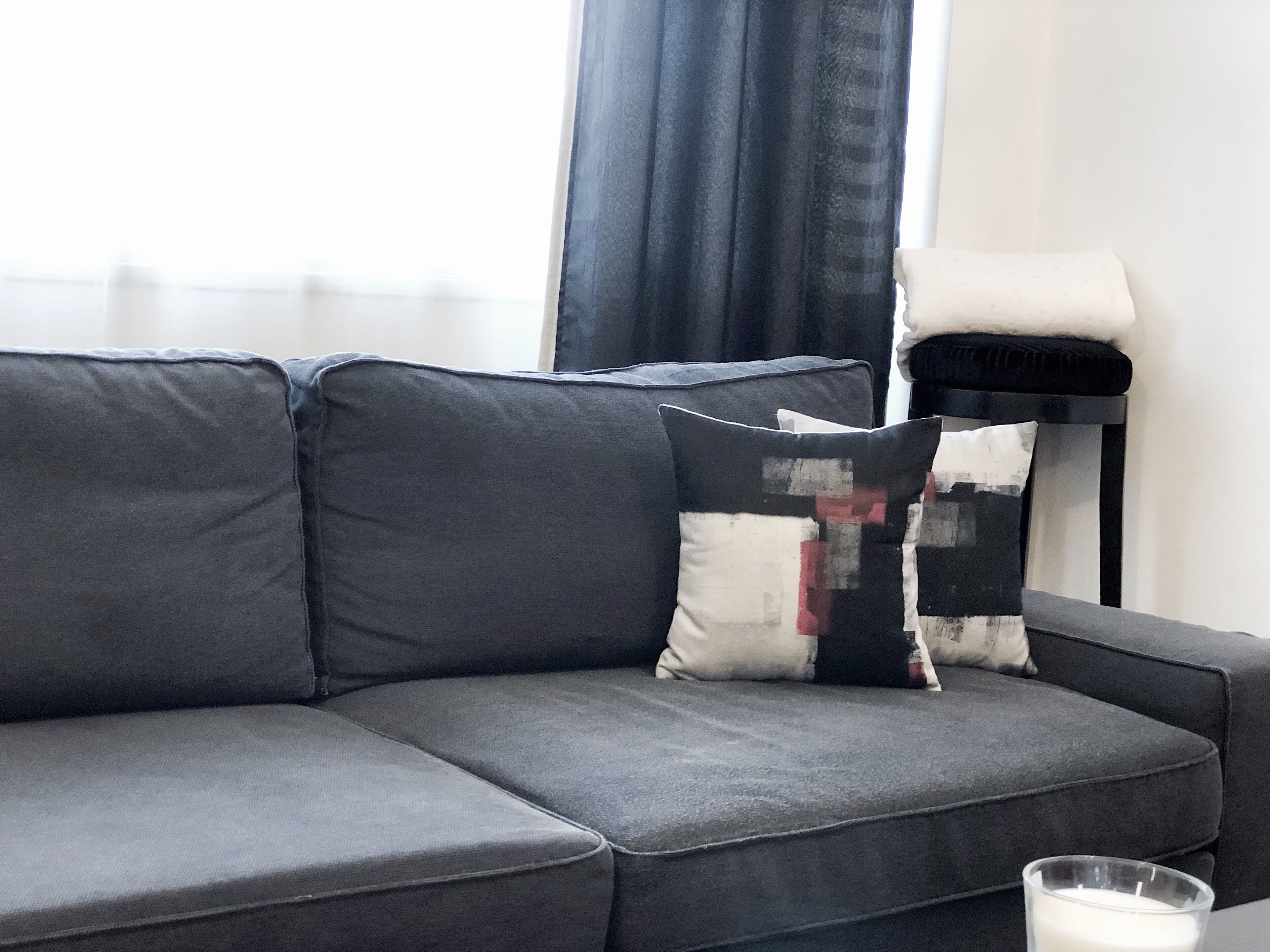 Een grijze modulaire bank met twee gekleurde kussens en een glazen kaars op een bijzettafeltje.