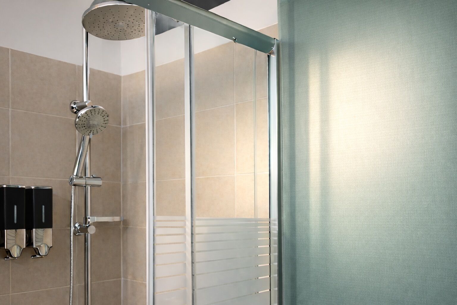 A modern shower enclosure with a rain showerhead and a handheld showerhead, a towel rack, and a glass door.