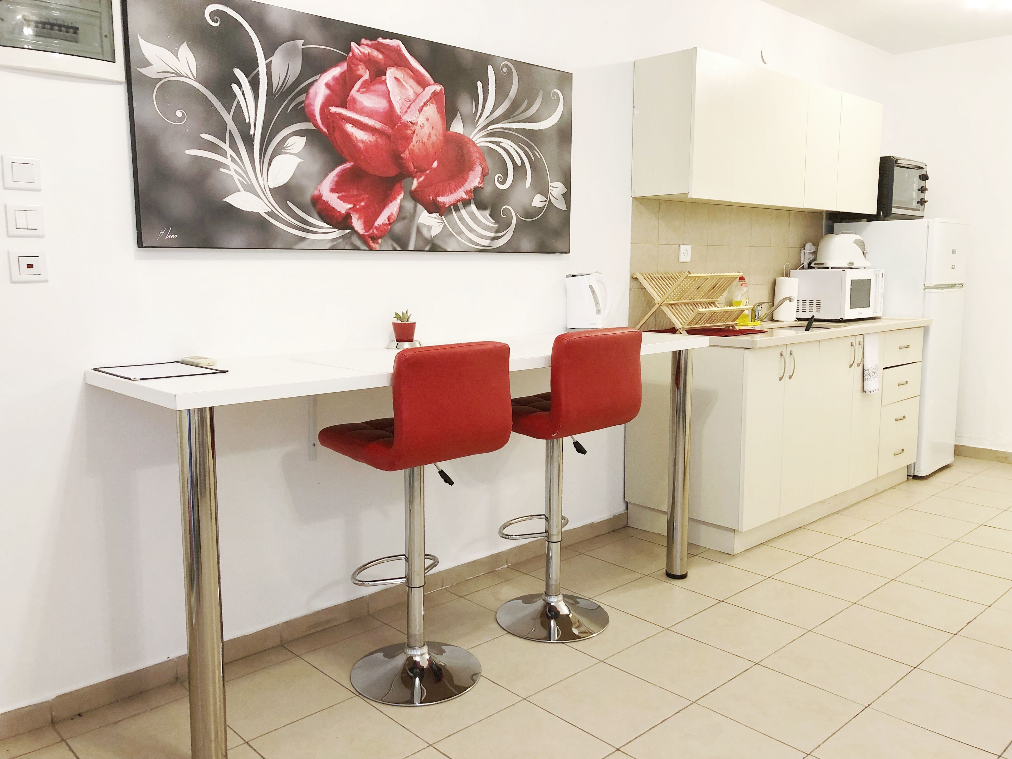 A modern kitchen with white cabinets, a microwave, a toaster, and a red flower painting on the wall.