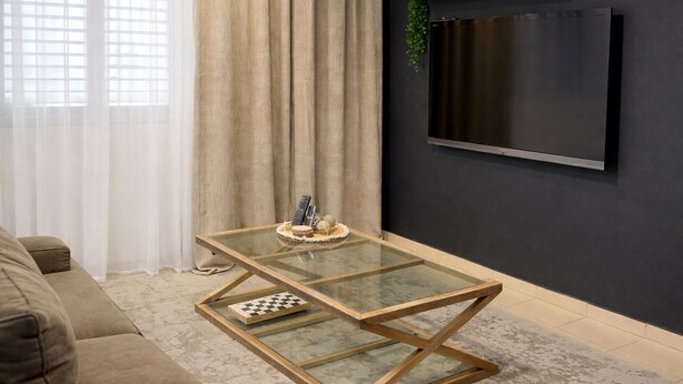 Una sala de estar moderna con una mesa de centro de vidrio, un sofá, un televisor montado en la pared y una cortina.