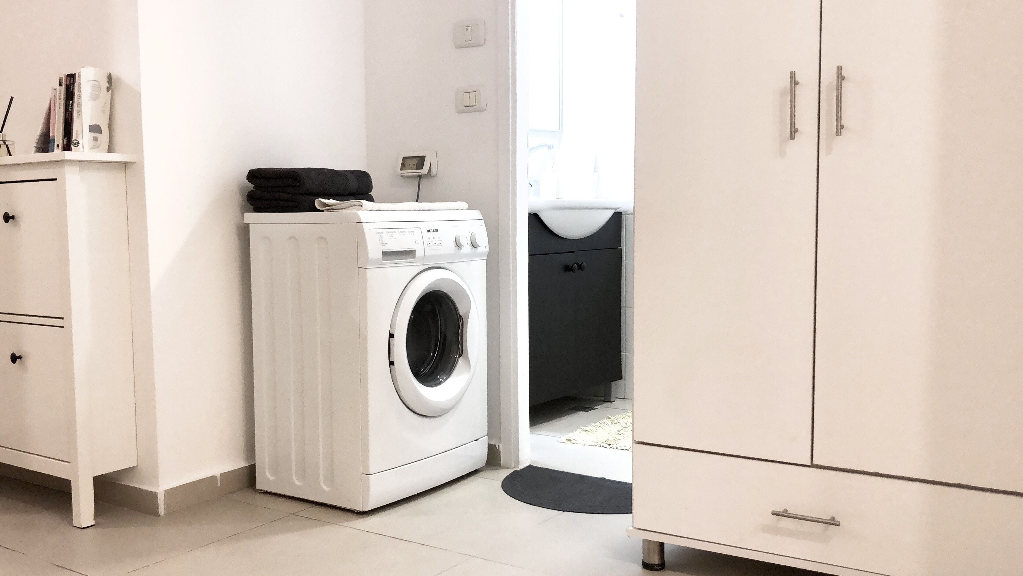 A laundry room with a front-loading washing machine, a cabinet, and a trash bin.