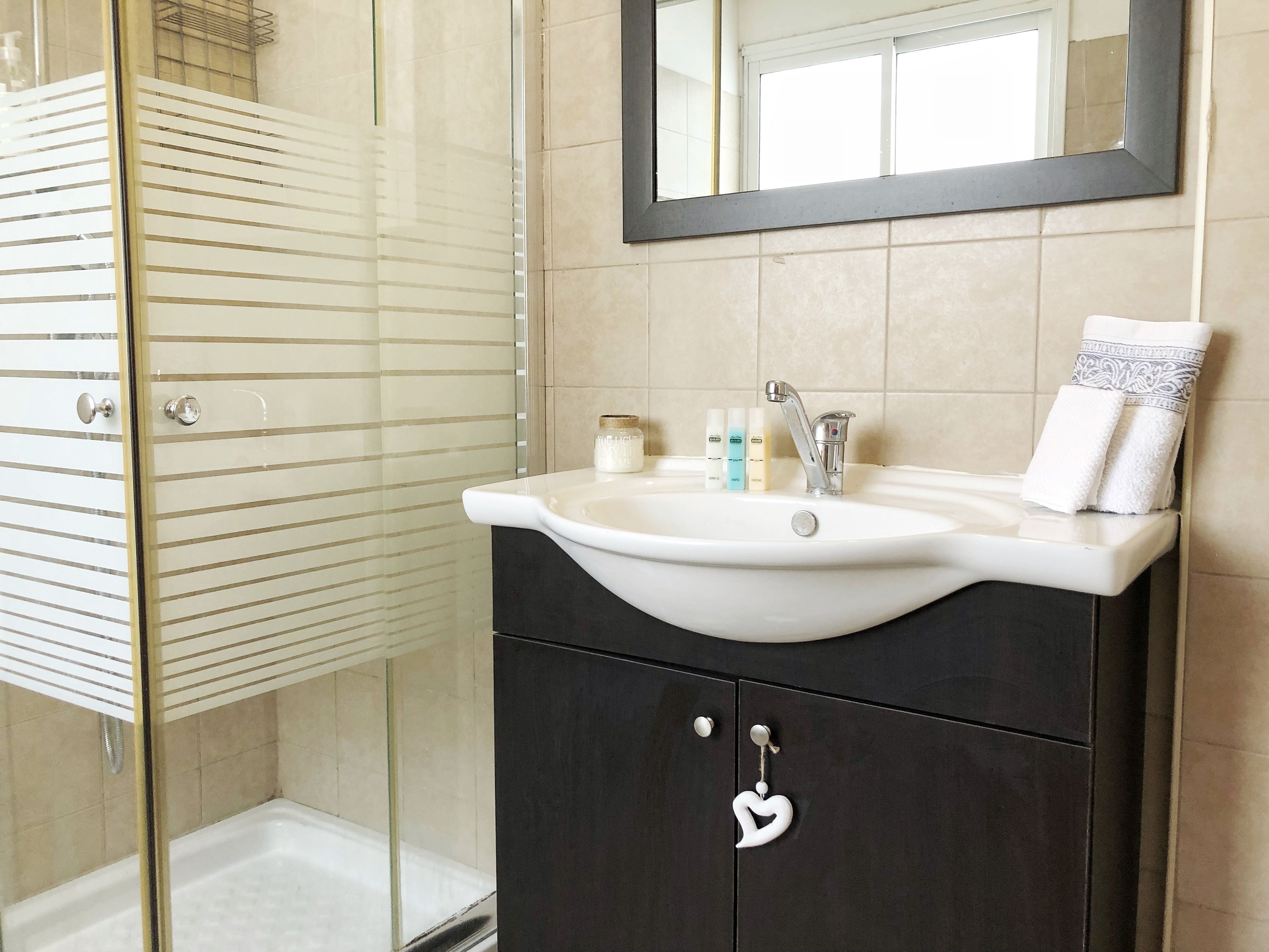 A bathroom with a glass shower enclosure, a white sink with a mirror above it, and toiletries on the sink.