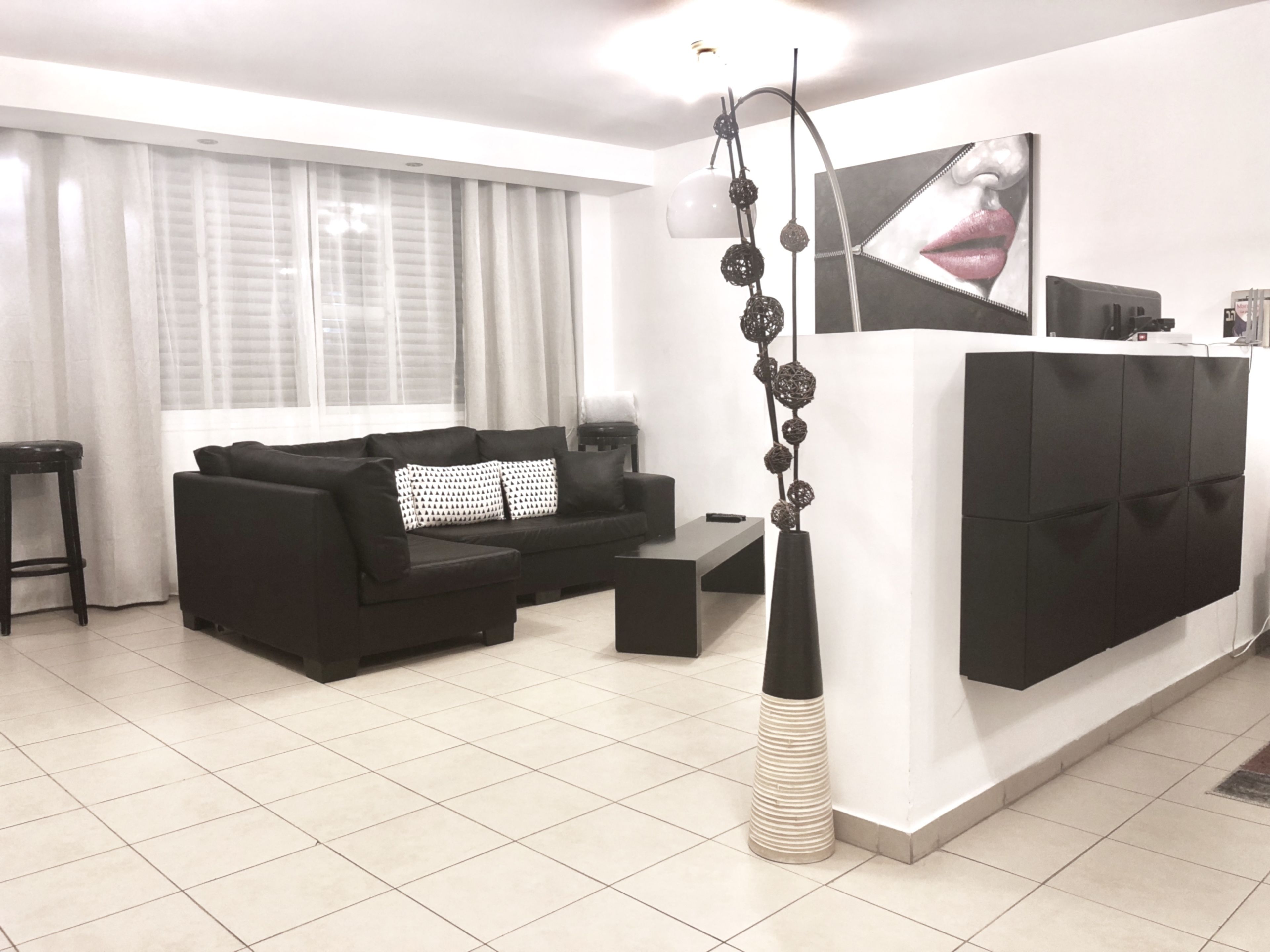 Un salon moderne avec un canapé noir, une table basse blanche et un vase décoratif.