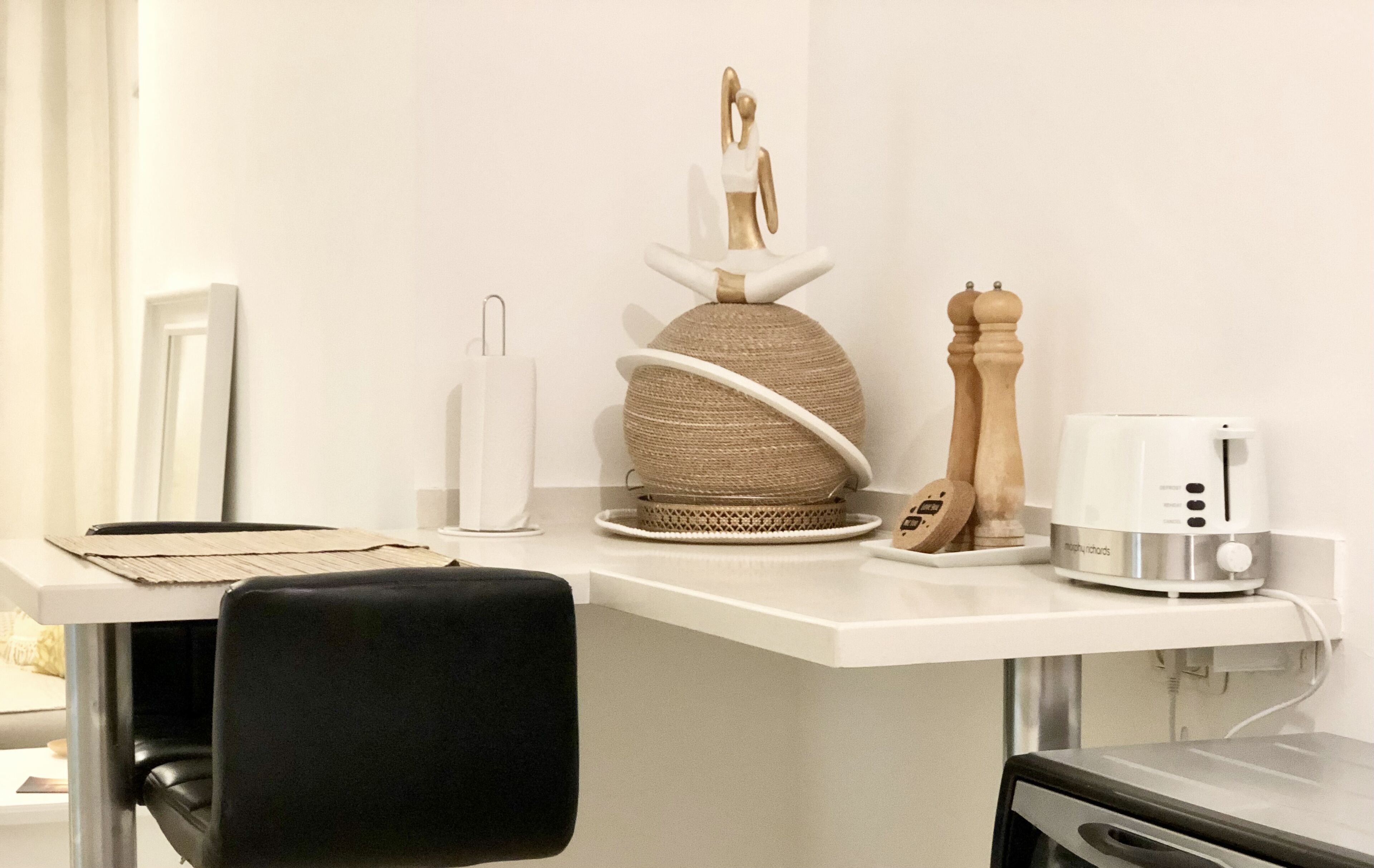 A modern kitchen with a white countertop, a coffee maker, a woven basket, and a wooden pepper mill.