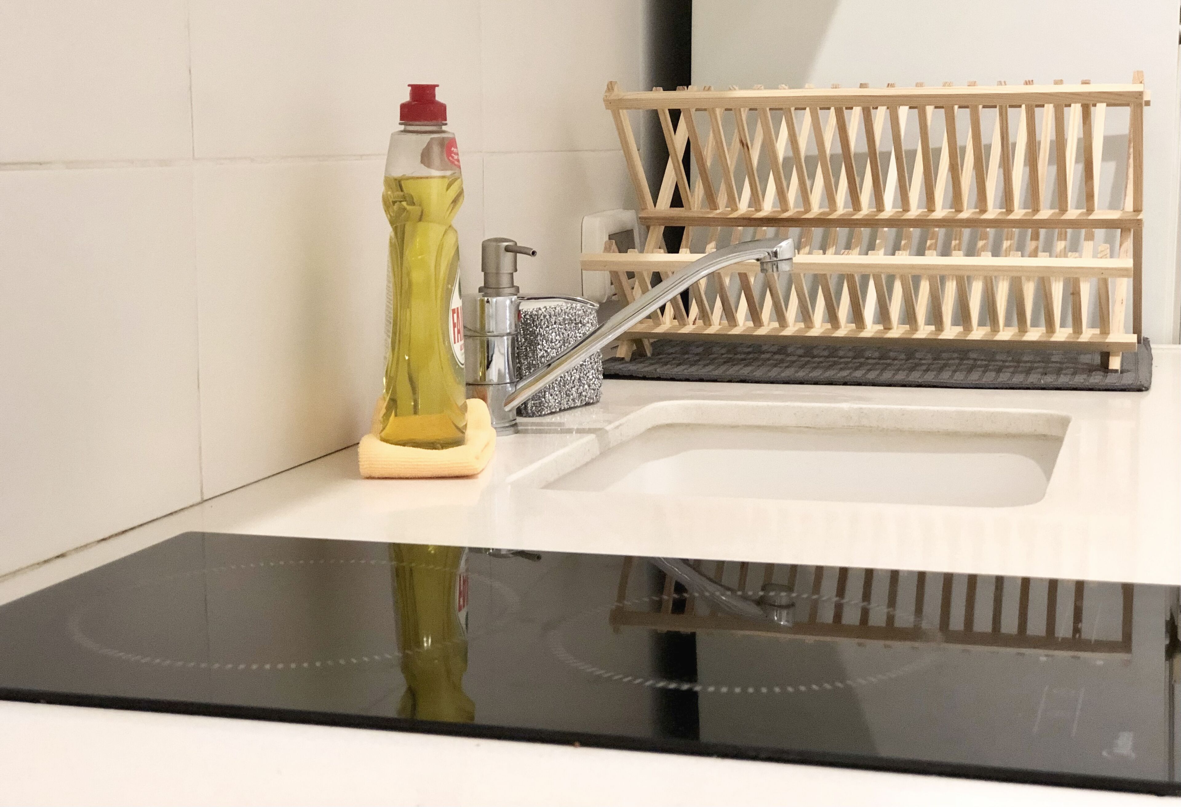 A modern kitchen with a black induction cooktop, a stainless steel sink, and a wooden drying rack.