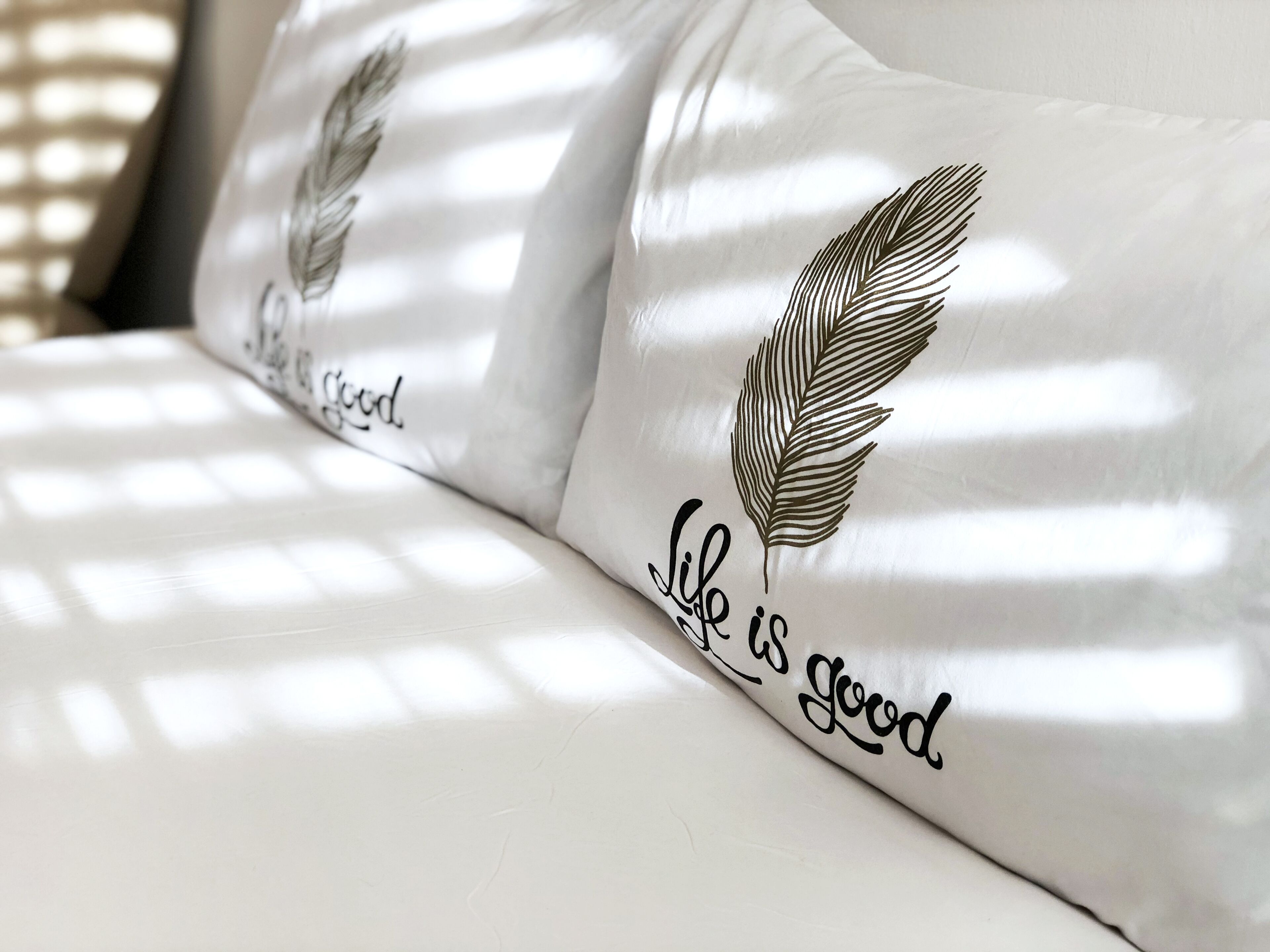 A white pillow with a feather design and the text "Life is good."