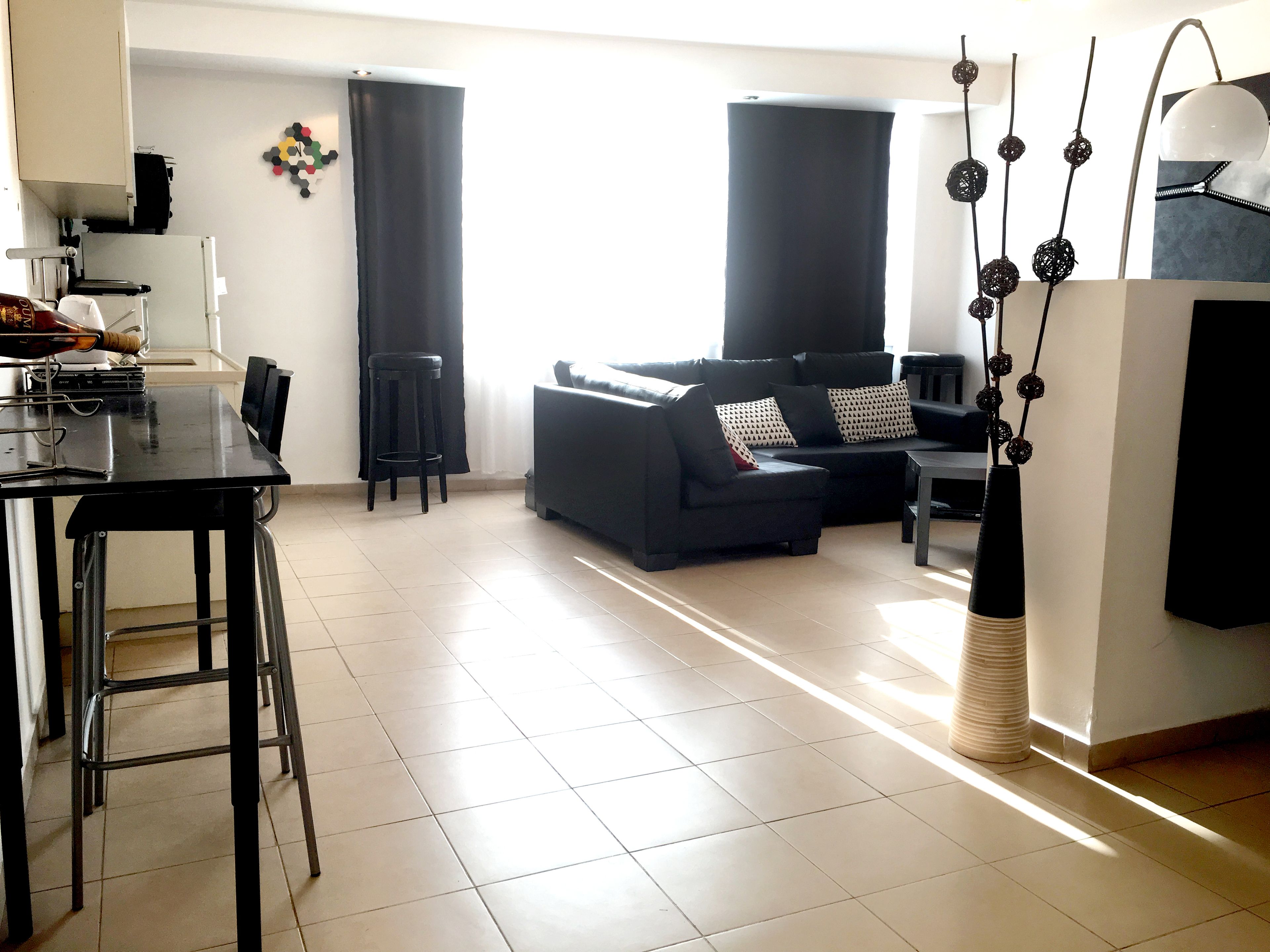 Un espacio moderno de sala con un sofá negro, una mesa de comedor con sillas y una cocina que incluye un refrigerador y armarios.