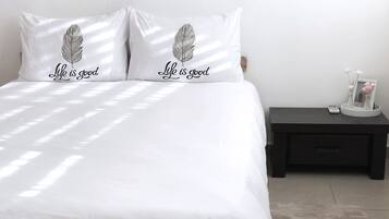Una cama con ropa de cama blanca y dos almohadas con un diseño de plumas y el texto "Life is good".