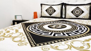 Una cama con colcha estampada en blanco y negro, dos almohadas a juego y una mesita de noche con lámpara y un cuadro enmarcado.