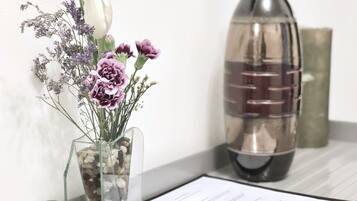 A clear glass vase with flowers and pebbles on a white surface next to a metal bottle and a document.