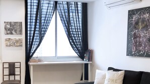 Una sala de estar moderna con un sofá negro, una mesa redonda blanca, una ventana con cortinas negras, un aire acondicionado instalado en la pared y un cuadro abstracto enmarcado.