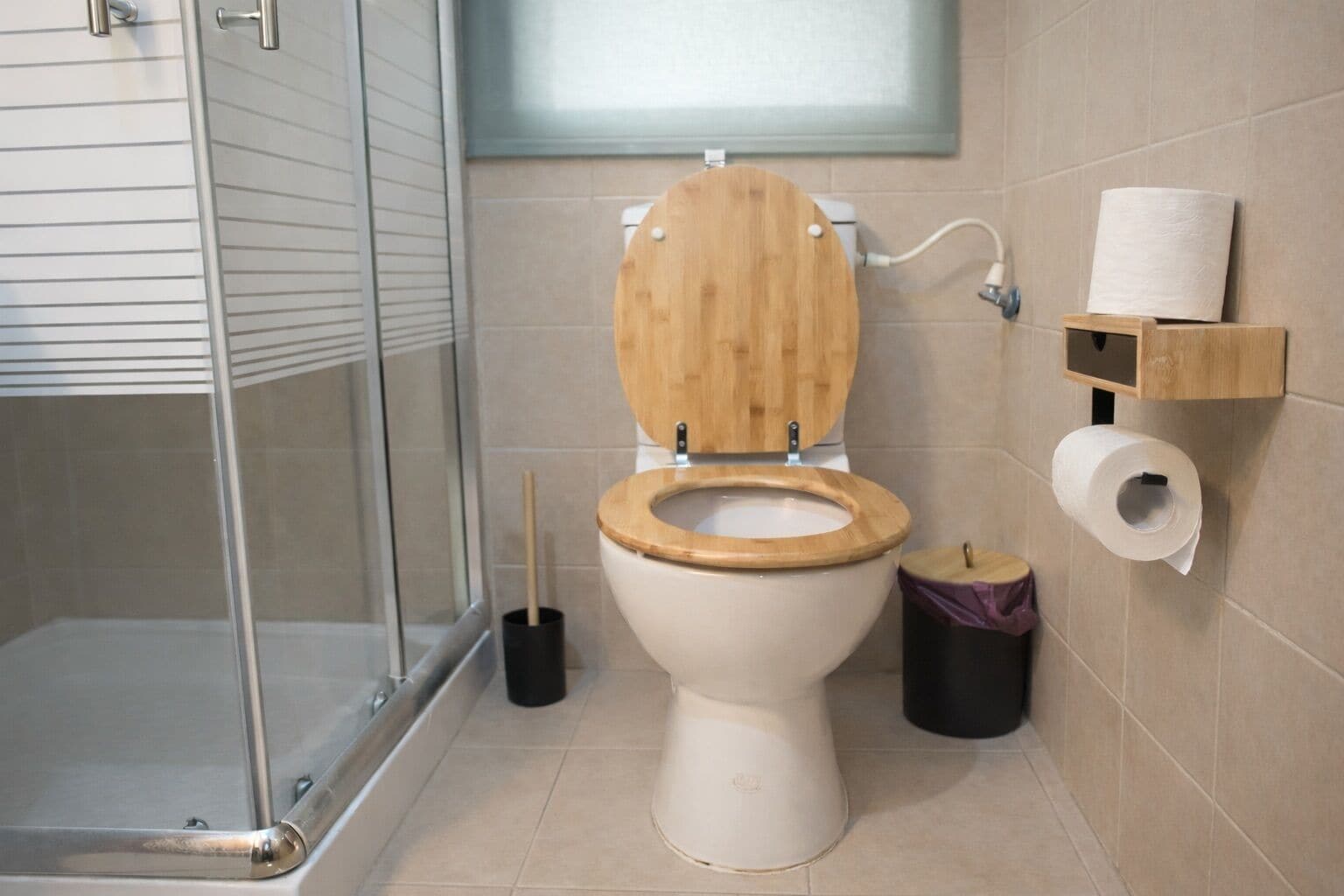 A bathroom with a wooden toilet, a glass shower enclosure, and a toilet paper holder on the wall.
