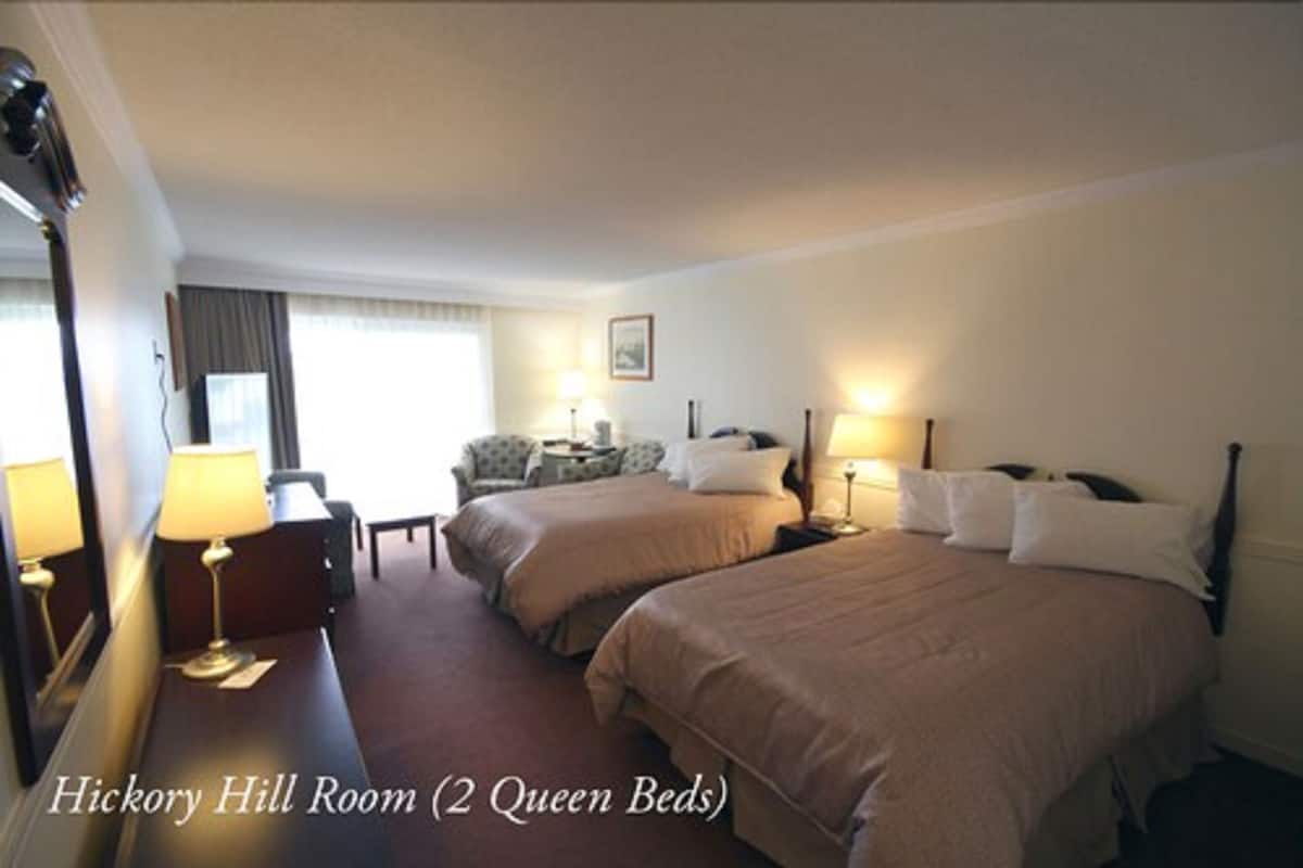 A hotel room with two queen beds, a desk with a lamp, a chair, and a window with curtains.