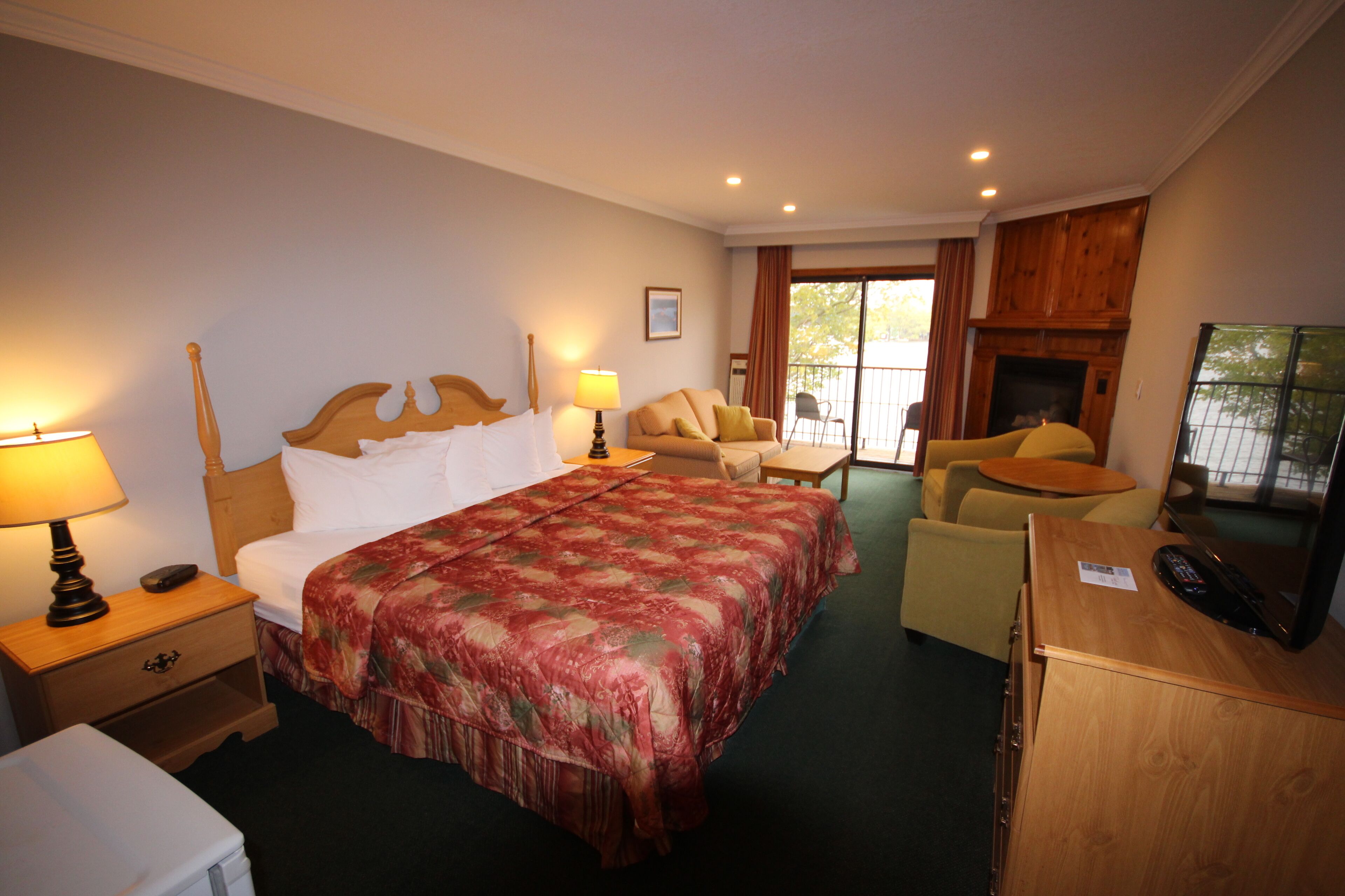 A hotel room with a large bed, a desk with a television, a chair, a sofa, and a fireplace.