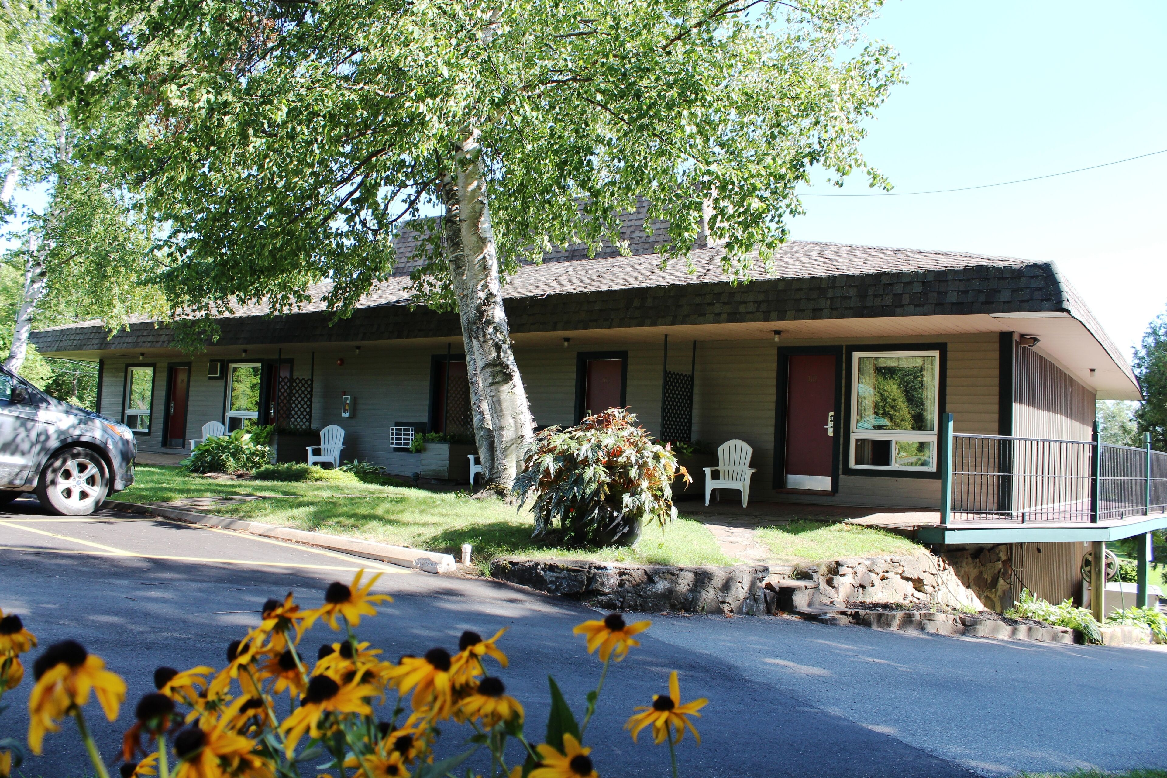 A motel with a two-story structure, a covered porch, and a small front yard with a tree and a flower bed.