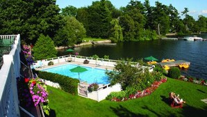 A swimming pool surrounded by lush greenery and a dock with boats. - The Glen House Resort (Leeds and the Thousand Islands)