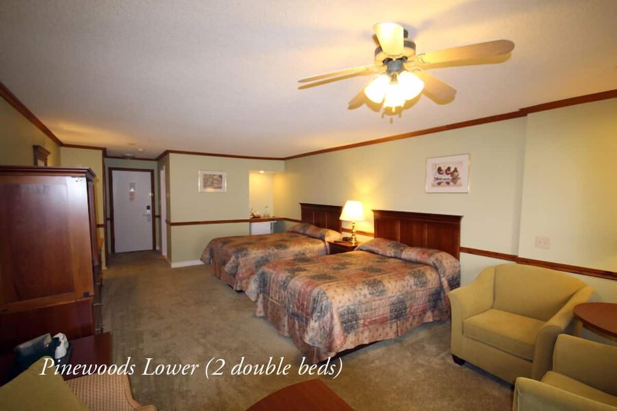 A Pinewoods Lower room with two double beds, a ceiling fan, a desk, and a chair.