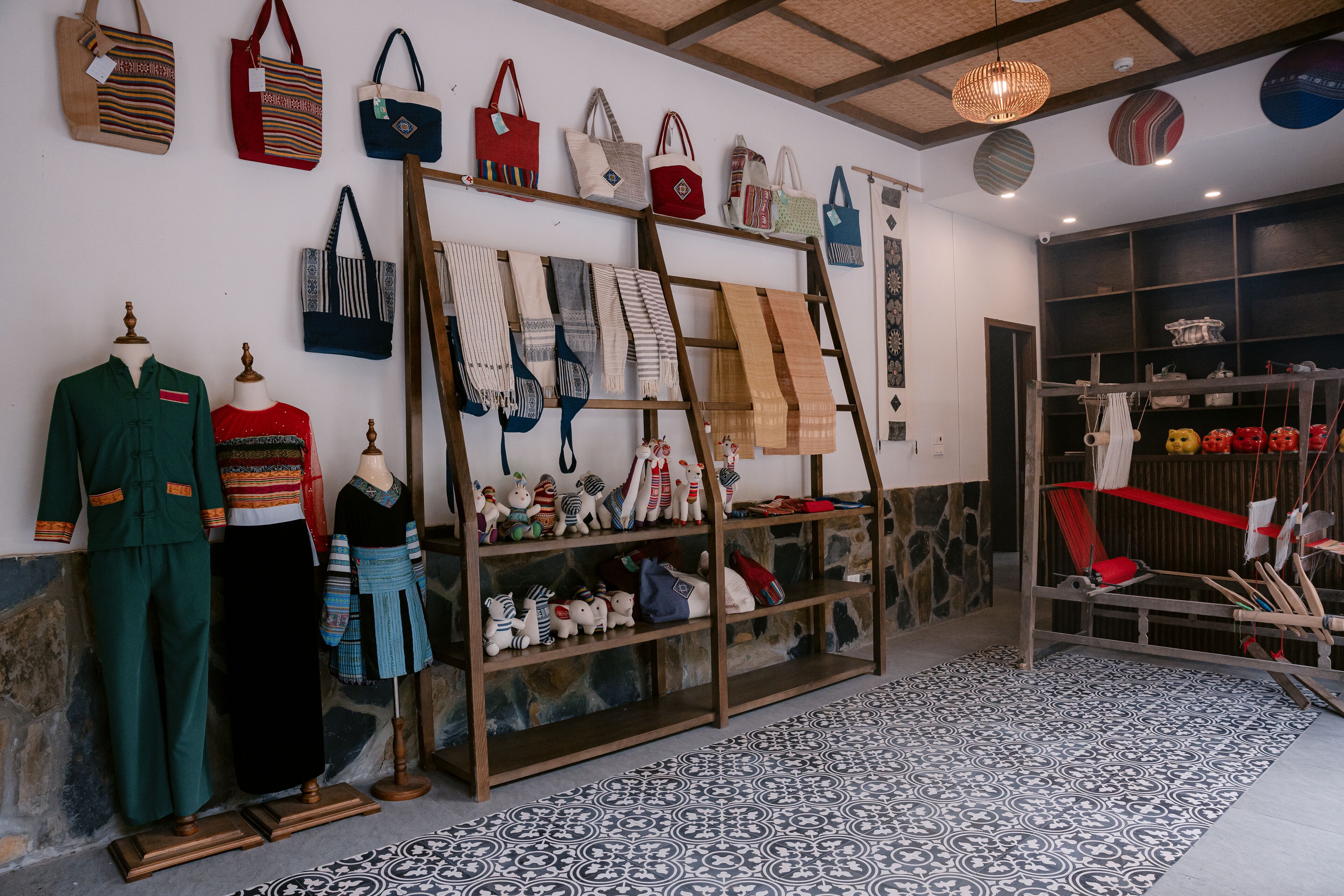 A boutique hotel interior with a display of bags and clothing on shelves, a patterned floor, and a stone wall.