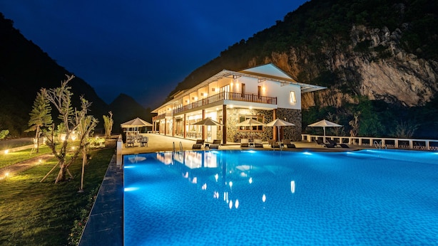 Et hotel med swimmingpool, udendørs siddepladser og et bjerglandskab i baggrunden.