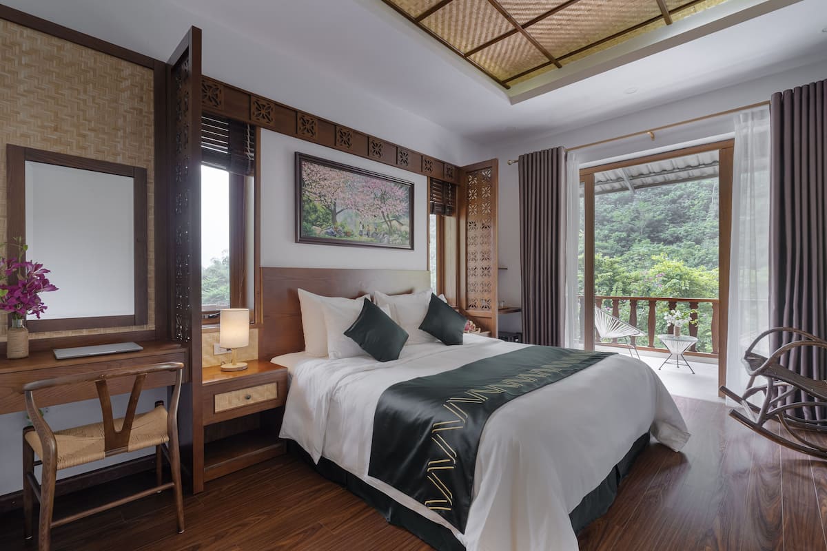 A bedroom with a bed, desk, chair, and a balcony with a view of greenery.
