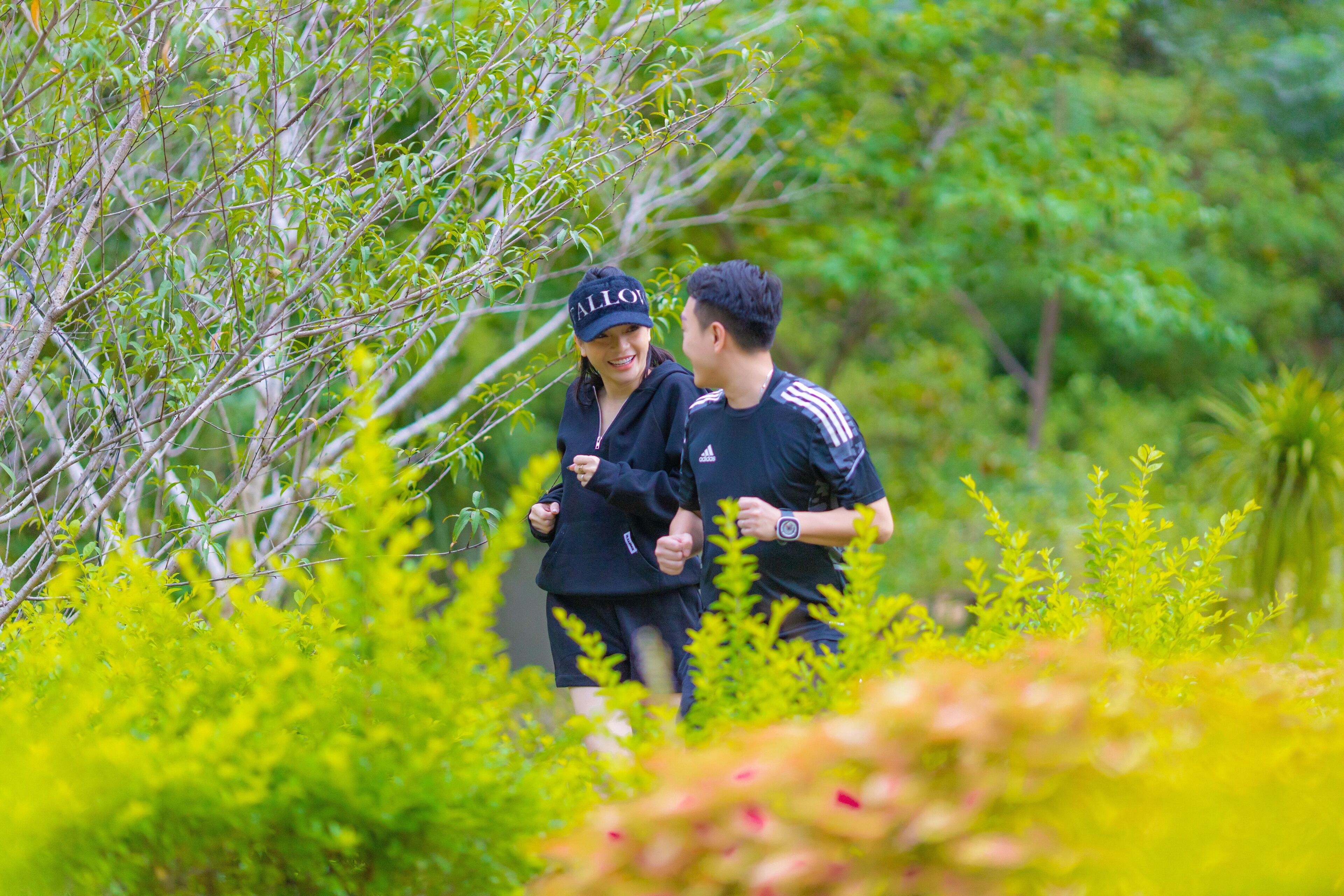 Two people walking in a lush, green outdoor area with dense foliage and trees.