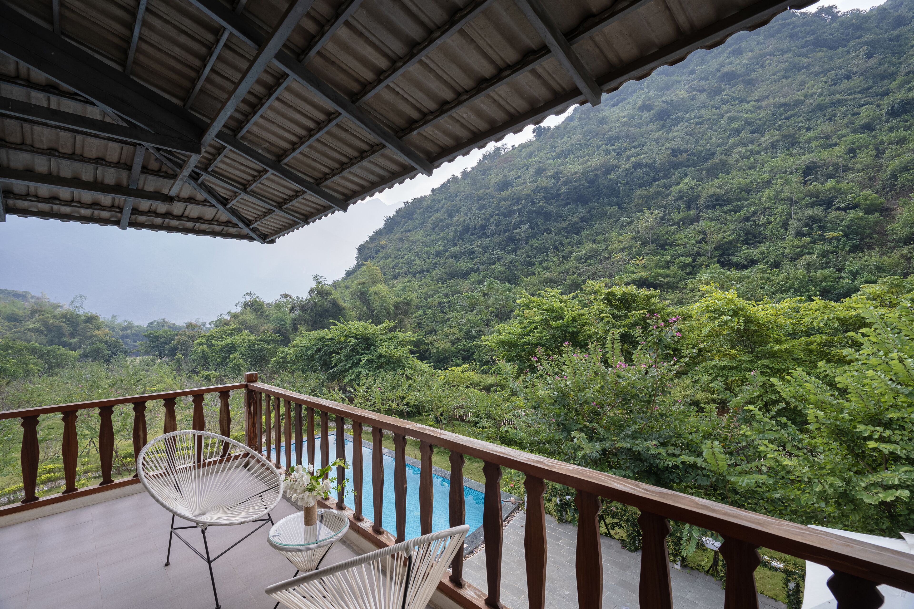 Un balcón con vistas a una ladera verde exuberante y una piscina.