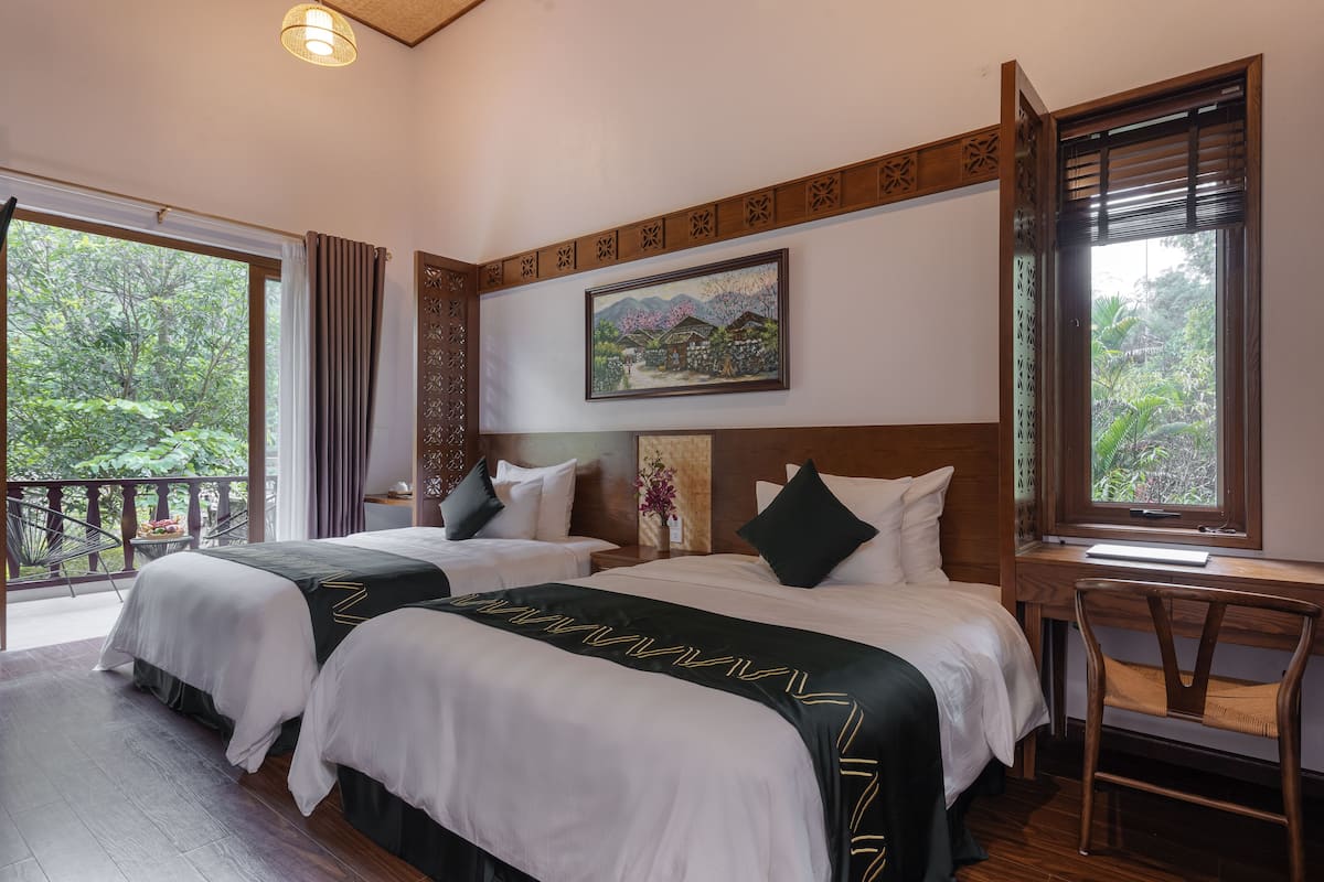 A hotel room with two beds, a desk, and a view of the outdoors.