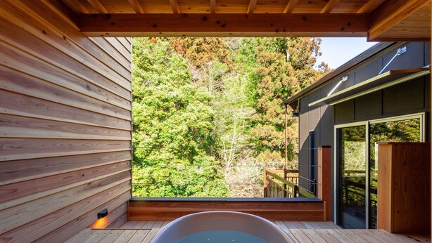 A wooden deck with a hot tub, a wooden wall, and a view of a forest.