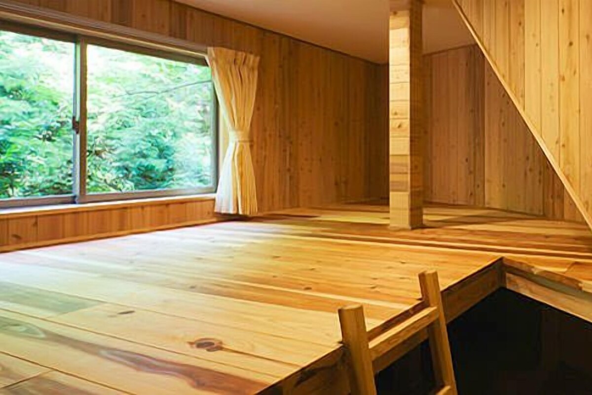 Une pièce aux murs en bois et au plafond en pente, une fenêtre avec des rideaux et une table en bois.