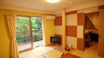 A room with a sliding glass door leading to a balcony, a television, a futon bed, and a wooden ladder.