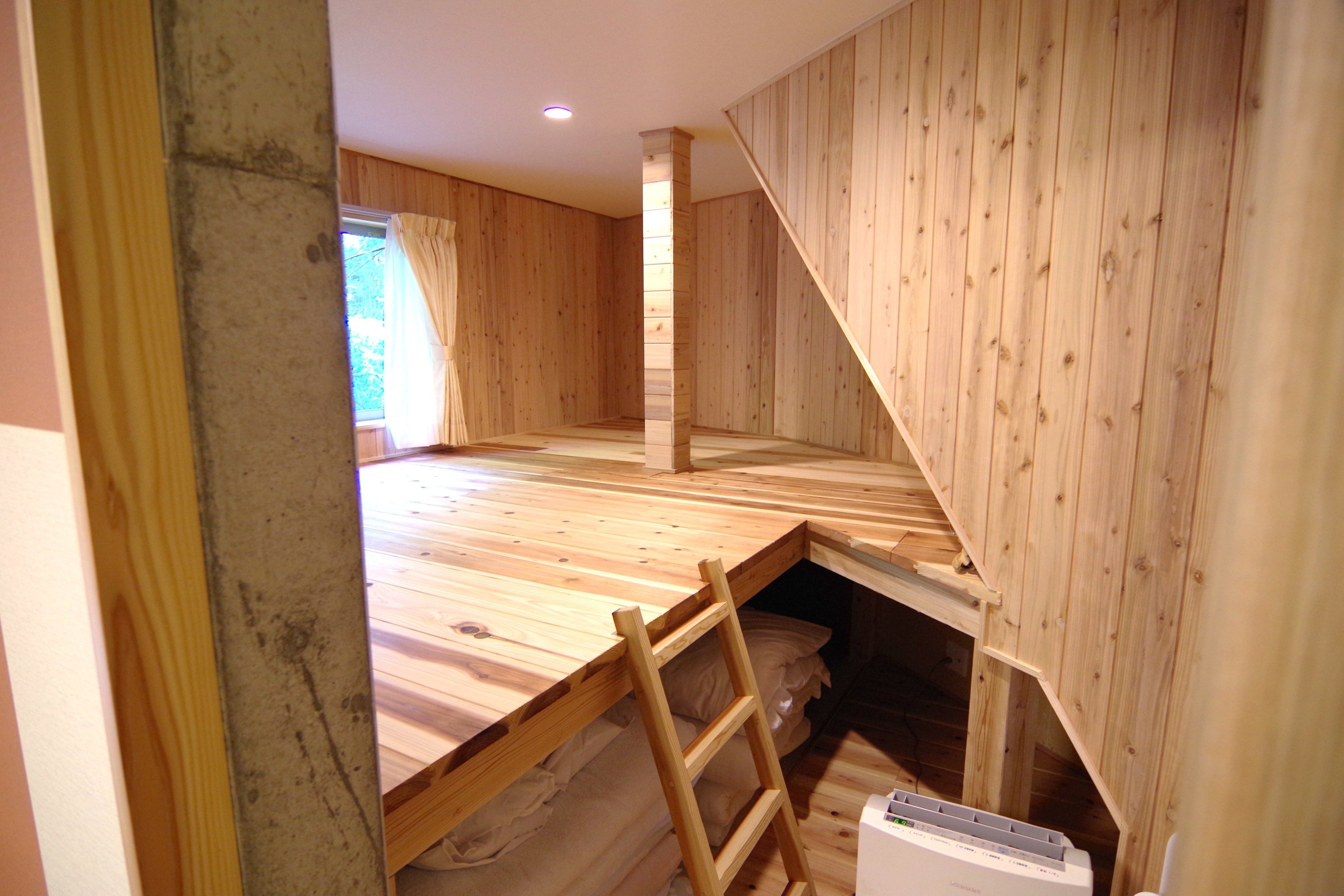 A room with wooden walls and a sloped ceiling, a wooden ladder, and a white appliance on the floor.