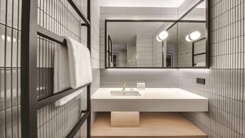 A modern bathroom with a large mirror, white tiled walls, a wooden vanity, and a towel rack.