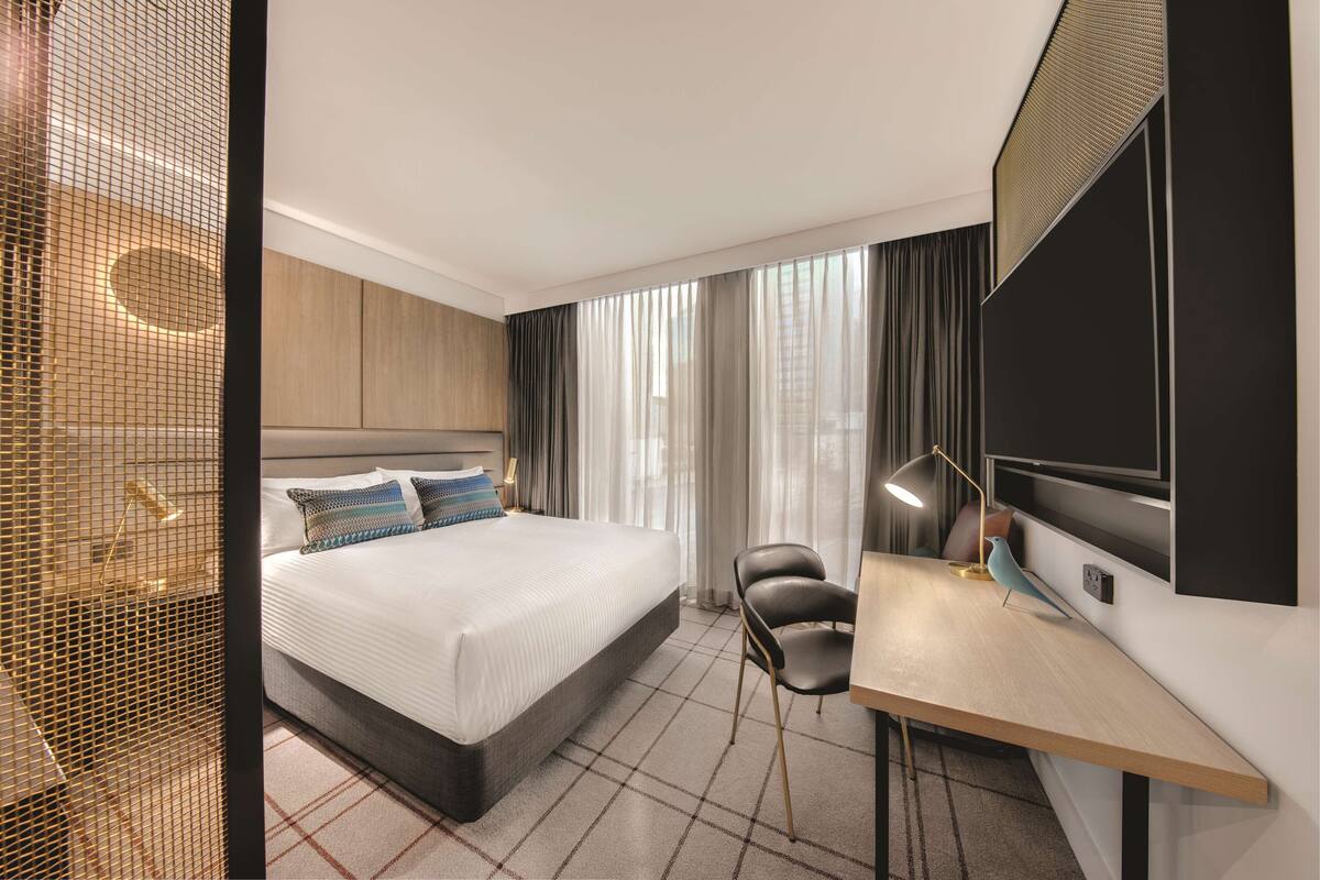 Een moderne hotelkamer met een groot bed, een bureau, een stoel en een aan de muur bevestigde televisie.