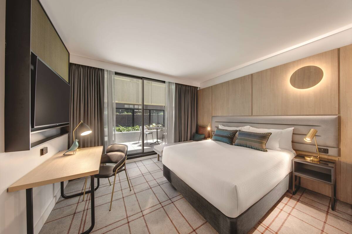 Een moderne hotelkamer met een groot bed, een bureau, een stoel, een televisie en een raam met gordijnen.