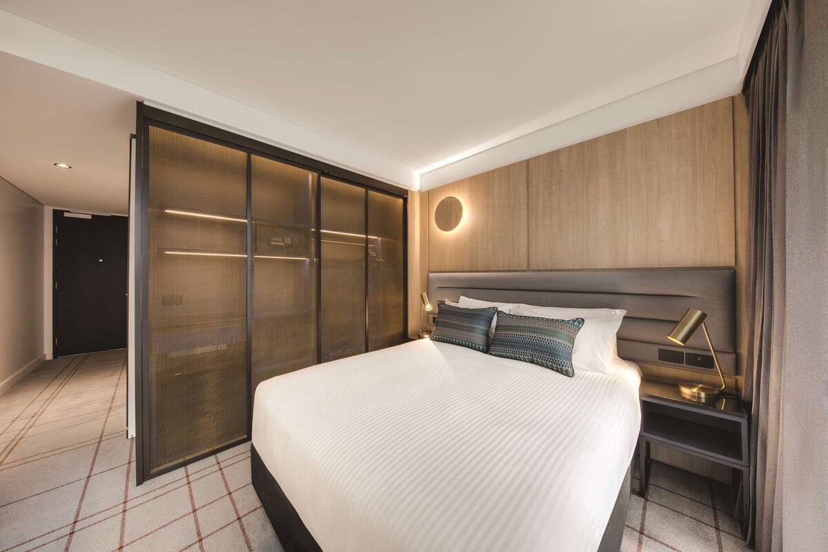 Een moderne hotelkamer met een groot bed, een inloopkast en een nachtkastje met een lamp.