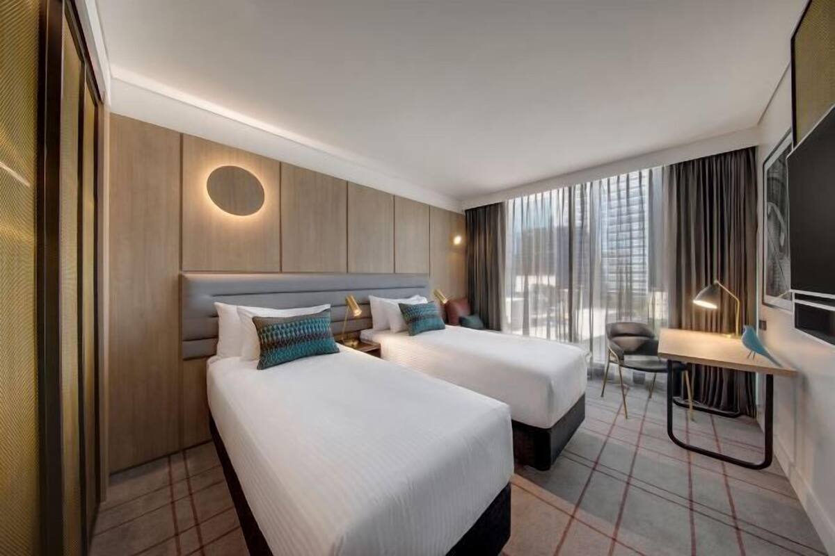 Een hotelkamer met twee bedden, een bureau, een stoel, een televisie en een groot raam met gordijnen.