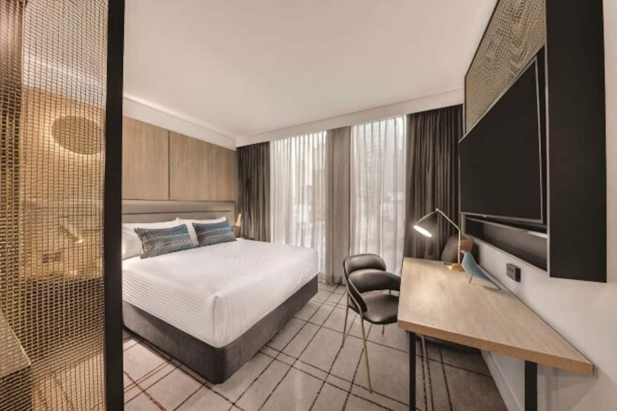 A modern hotel room with a large bed, a desk, and a chair.