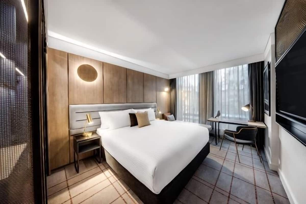 A modern hotel room with a large bed, a desk, and a view of the city.
