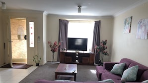 A living room with a sofa, coffee table, TV, and decorative plants.