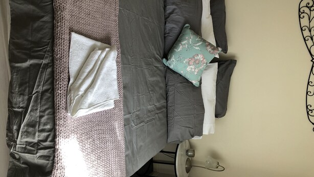 A neatly made bed with a grey duvet, white pillows, and a floral pillow.